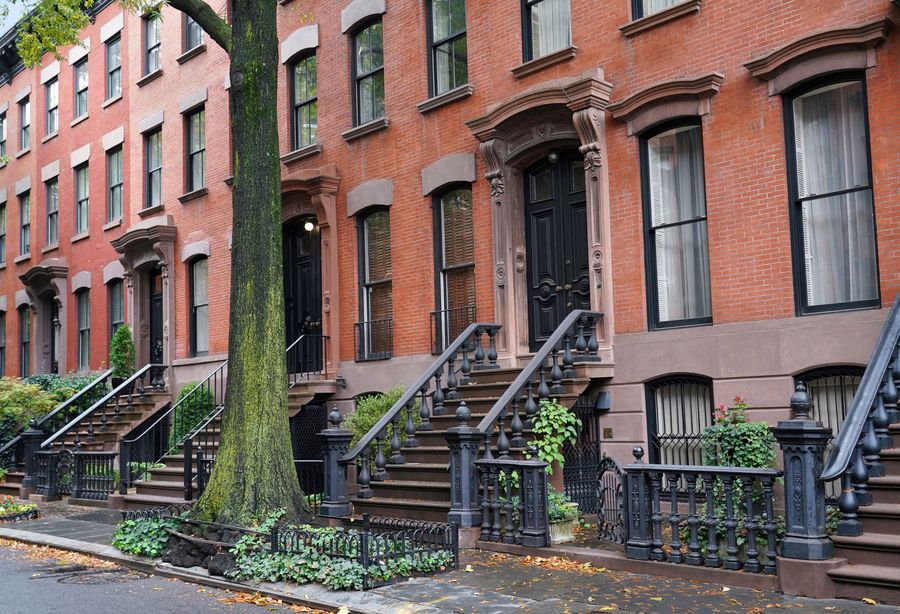 Row of classic New York brownstone townhouses with iron stoops and street trees
