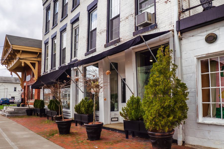 Charming small-town street with white brick storefronts, black awnings and potted evergreens