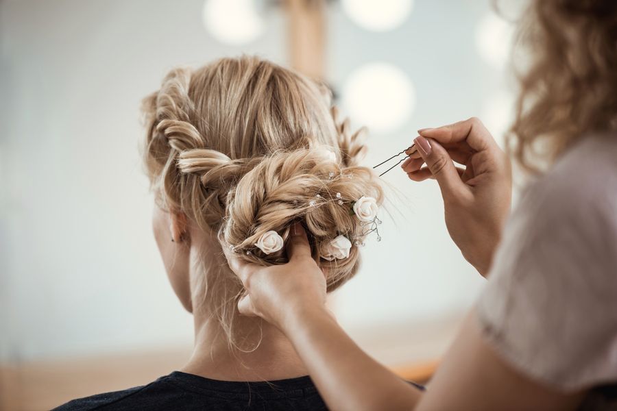 Stylist pinning tiny flowers into a braided blonde bridal updo