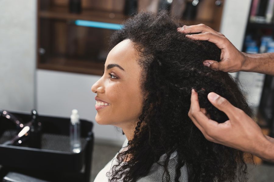 Smiling woman with long natural curls as her stylist lifts and shapes her hair at the wash station