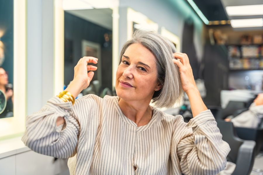Smiling woman with a silver bob running her hands through her hair in a salon