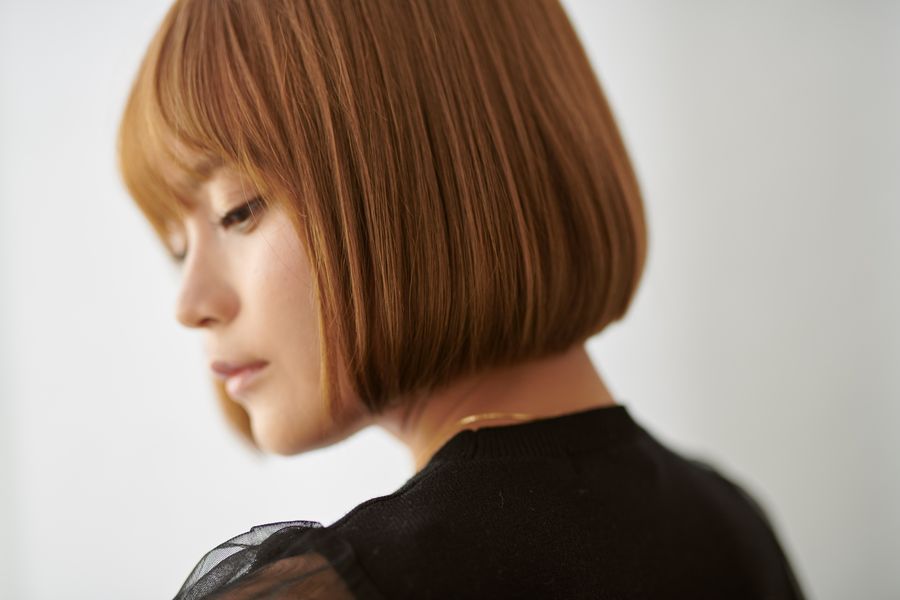 Woman with a sleek copper-brown bob and blunt bangs, shown in soft profile on white